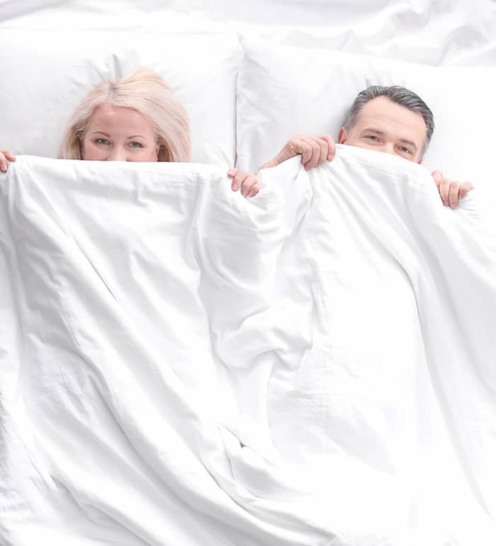Senior couple hiding under blanket in bed together, top view