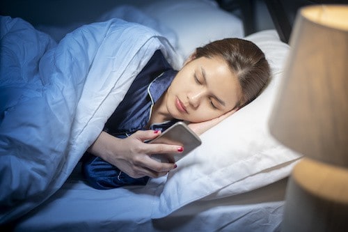 Beautiful woman is playing smart phone before sleep in bedroom
