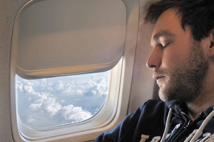 young man sleeping on a plane in the window seat