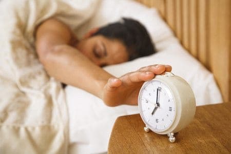 woman hits snooze button on alarm clock